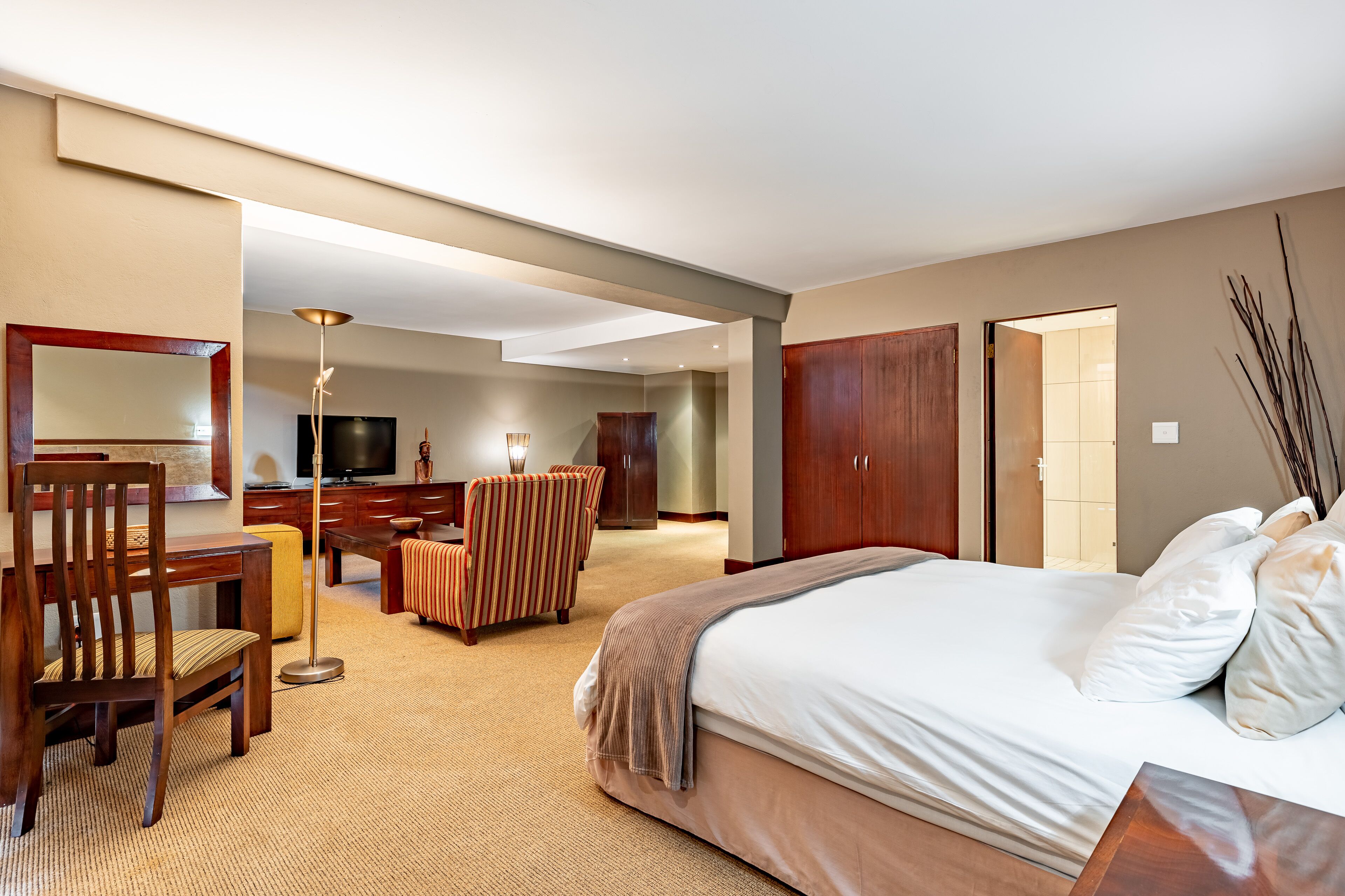 A hotel room with a large bed, a desk, a chair, a TV, and a wardrobe.