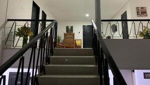 Una escalera con barandilla, una puerta al final y una planta a la izquierda.