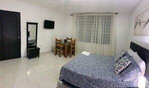 A bedroom with a bed, a desk, a chair, a TV, and a window with curtains. - HOSTAL RINCON DE GRANADA (Cali)