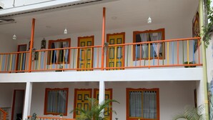 Un edificio de dos plantas con balcones, plantas en macetas y una fachada sencilla.