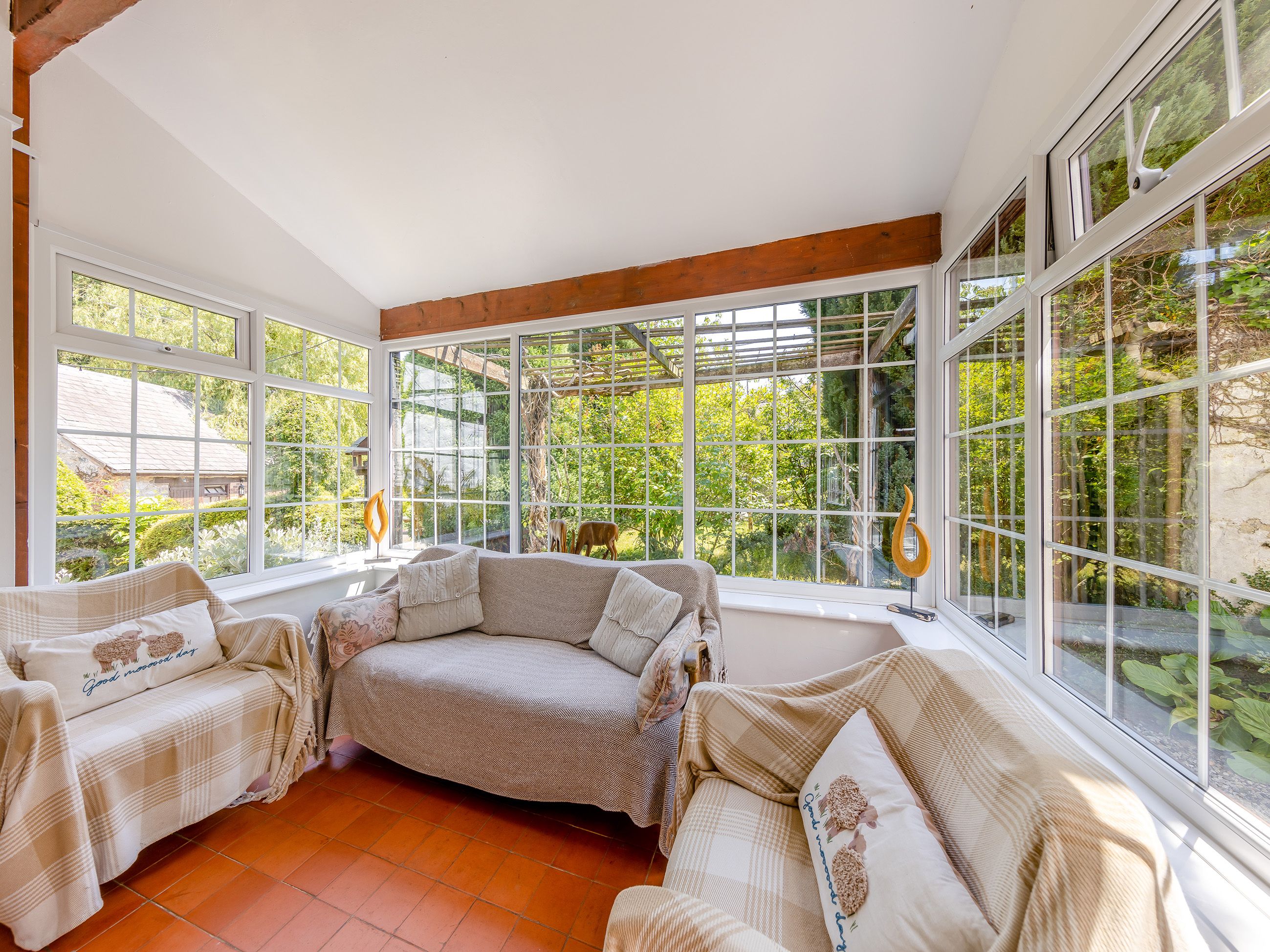 Ein gemütliches Zimmer mit großem Fenster, einem Holzbalken an der Decke und einem karierten Sofa.