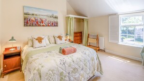 Een slaapkamer met een groot bed, een nachtkastje, een radiator, een raam met gordijnen en een schilderij aan de muur.