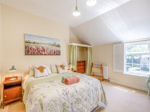 Ein Schlafzimmer mit einem großen Bett, einem Nachttisch, einem Heizkörper, einem Fenster mit Vorhängen und einem Bild an der Wand.