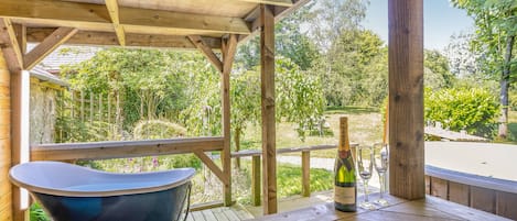 A wooden deck with a hot tub, a bottle of wine, and a picnic table.