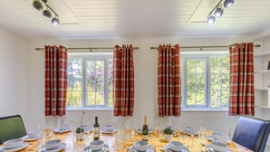 Ein Esszimmer mit Holztisch, gedeckt für sechs Personen, mit Fenstern mit Karomustertvorhängen.