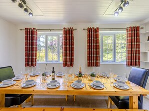 A dining room with a wooden table set for six, flanked by windows with plaid curtains. - The Farmhouse - UKC6678 (Betws Yn Rhos)
