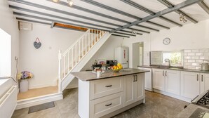 Een moderne keuken met witte kasten, een centraal eiland en een trap naar een hoger niveau.
