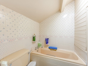 Ein Badezimmer mit Badewanne, Toilette und Waschbecken. Auf dem Waschbecken liegen Pflegeprodukte und über der Badewanne ist eine Duschstange angebracht.