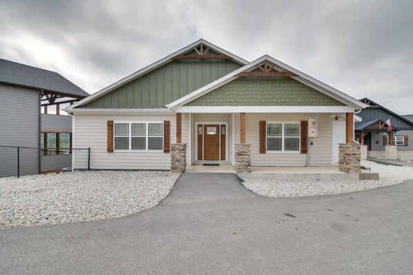 A two-story house with a front porch, stone pillars, and a gravel driveway. - Lake Views, Private Hot Tub, Indoor and Outdoor Pool, Playground, Sleeps 24! (Branson)