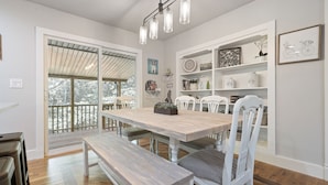 A dining area with a wooden table and white chairs, a bench, and a ceiling light fixture. - Bella's Vista - Hound Dog Haven (Bella Vista)