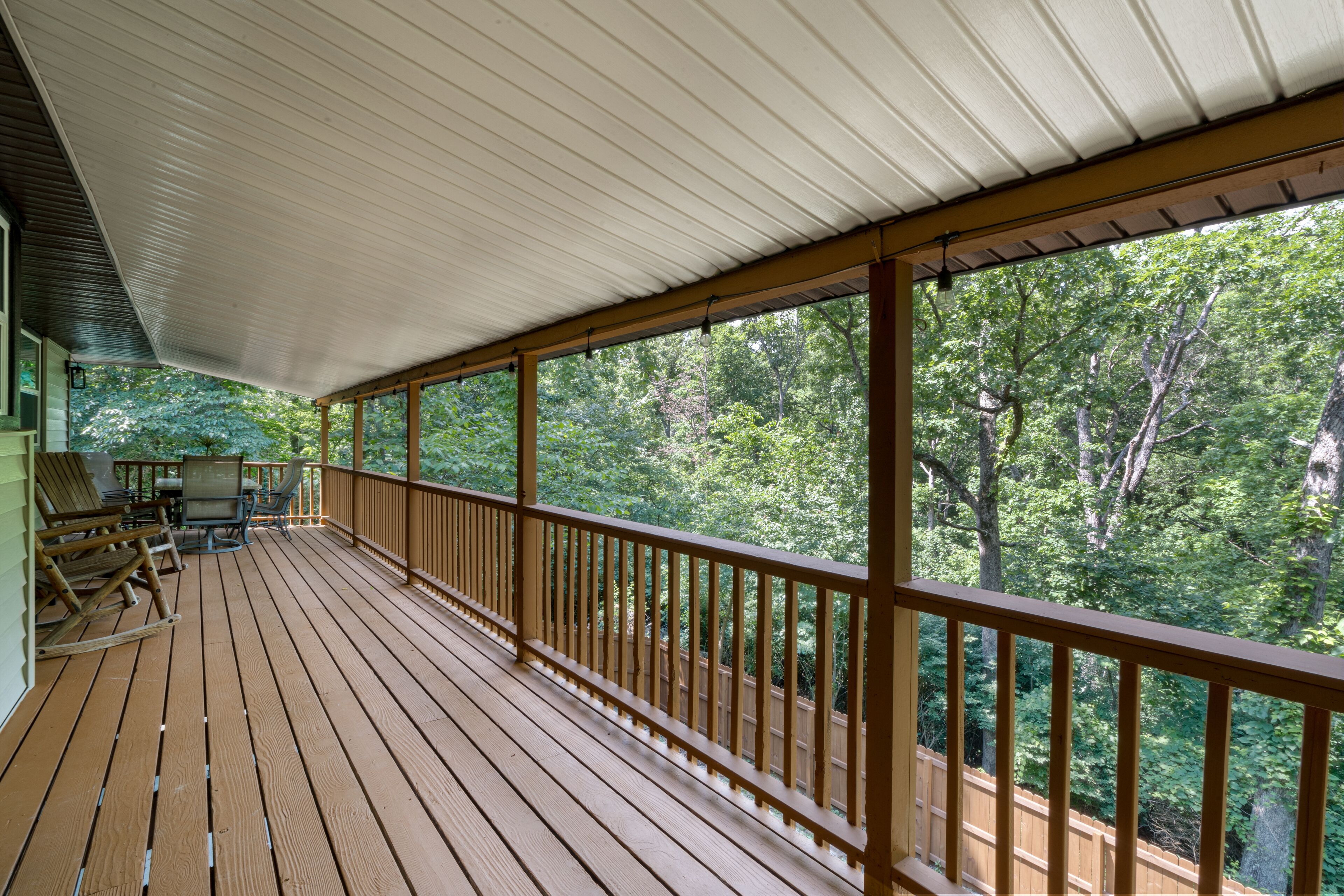 Une terrasse en bois surmontée d’un toit en métal, offrant une vue sur une zone boisée.