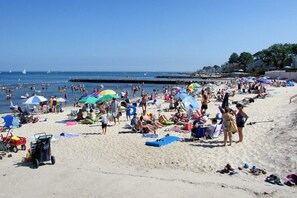 Een druk strand met mensen die zonnen, zwemmen en langs de kust wandelen.