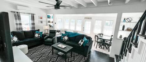 A modern living room with dark sofas, a patterned rug, and a ceiling fan.