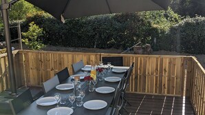 Un área de comedor al aire libre con una mesa dispuesta para seis personas, rodeada de piso de madera y un gran paraguas que da sombra.