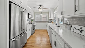 A modern kitchen with white cabinetry, stainless steel appliances, and a wooden floor. - Betty Boo - Channel House w/Pool in Cherry Grove (North Myrtle Beach)