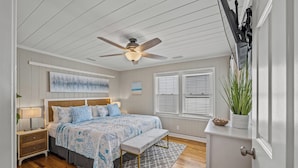 A bedroom with a bed, bedside table, lamp, ceiling fan, window blinds, and a potted plant. - Betty Boo - Channel House w/Pool in Cherry Grove (North Myrtle Beach)