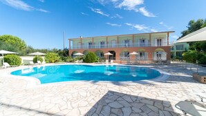 Ein Pool mit Liegestühlen und Sonnenschirmen, umgeben von einer Steinterrasse und einem Gebäude mit Balkonen.