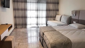 Ein Hotelzimmer mit Bett, Nachttisch, an der Wand befestigtem Fernseher und einem Fenster mit Vorhängen.