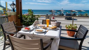 Ein Tisch, reichhaltig mit Frühstück angerichtet, mit einem Glas Orangensaft, und Blick auf Strand und Meer.