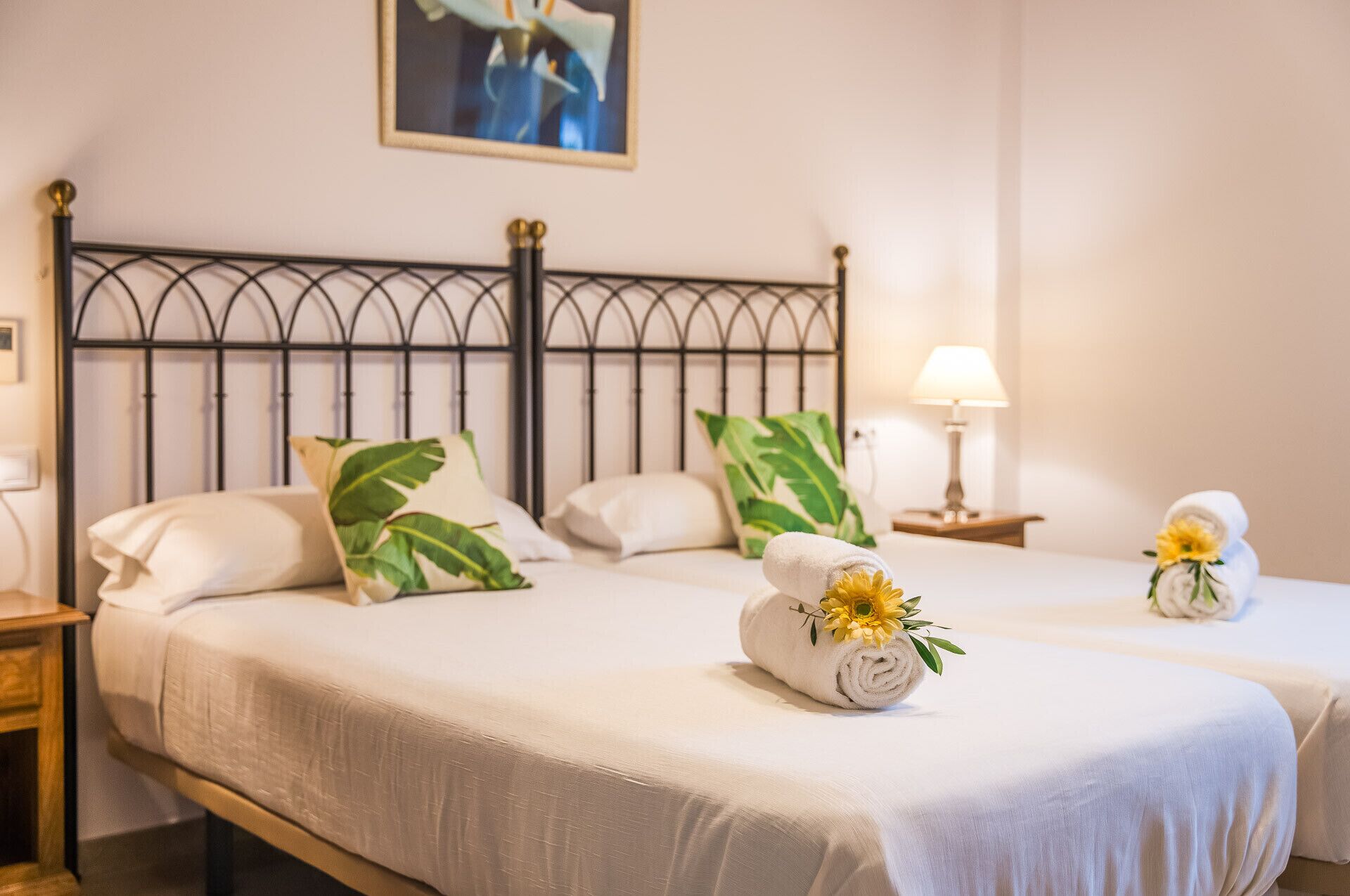 A hotel room with a bed, two pillows, a nightstand, a lamp, and a painting on the wall.