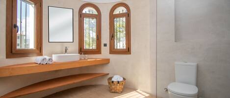 A bathroom with a curved wooden vanity, a white toilet, and a wicker basket with towels.