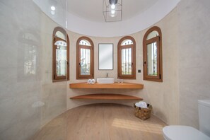 A modern bathroom with a curved vanity, a large mirror, and a wooden floor. - Adriana Di Levante (Zakynthos)