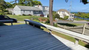 A wooden deck with a railing, overlooking a residential area with houses and a body of water.