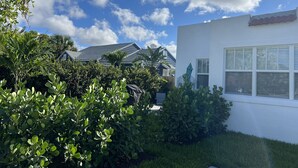 Un barrio residencial con un edificio blanco, abundante vegetación y un cielo azul despejado con nubes.