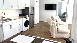 Una cocina moderna con armarios blancos, un refrigerador de acero inoxidable, una lavadora y un televisor de pantalla plana montado en la pared.