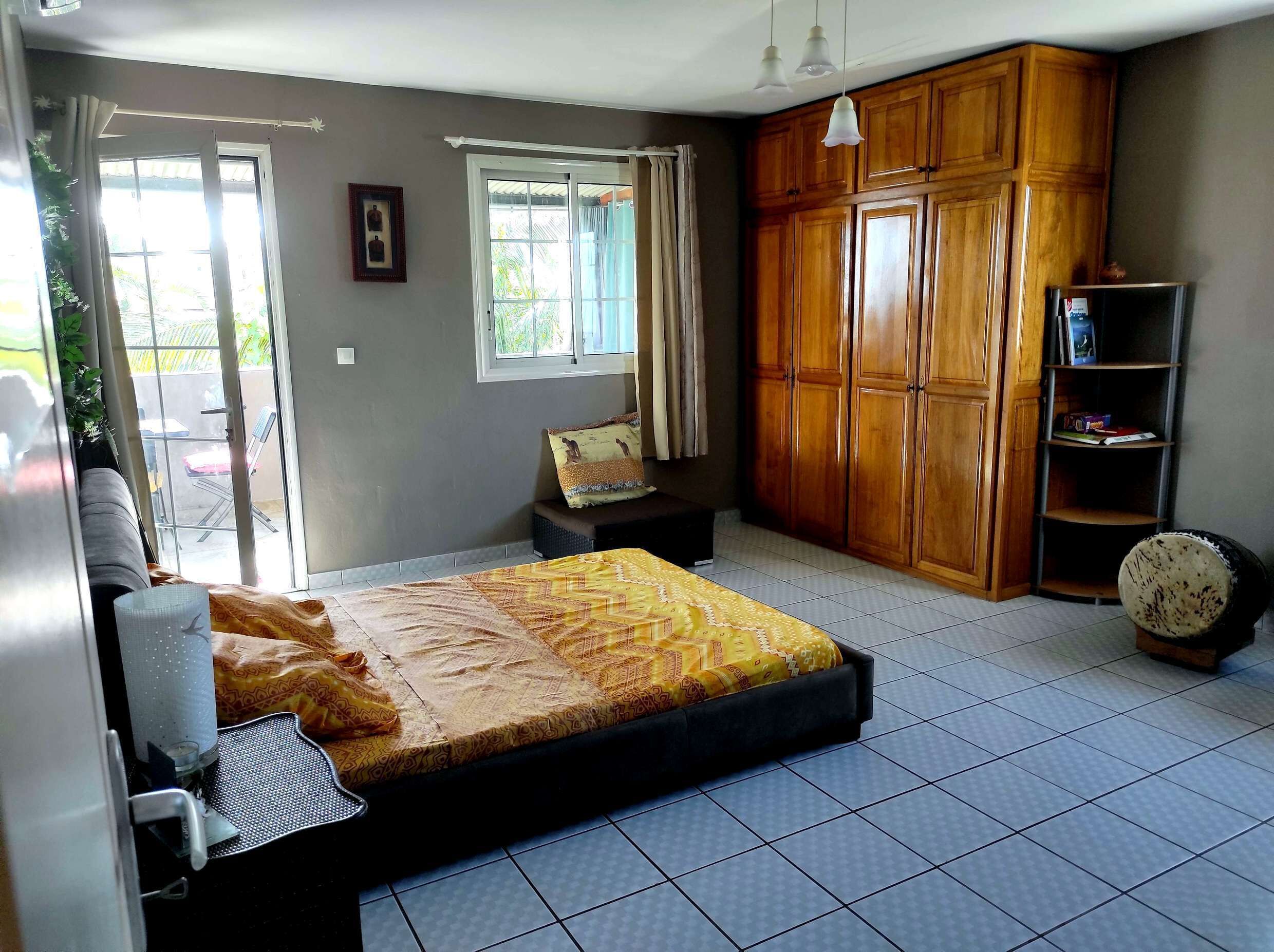 A bedroom with a bed, a wardrobe, a small bench, a bookshelf, and a sliding glass door leading to an outdoor area.