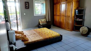 A bedroom with a bed, a wardrobe, a small bench, a bookshelf, and a sliding glass door leading to an outdoor area. - La Maison de Jo (Saint Paul)