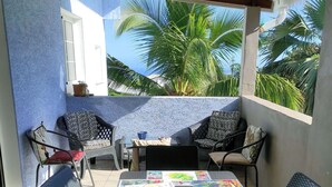 A covered outdoor seating area with a table, chairs, and a view of palm trees. - La Maison de Jo (Saint Paul)