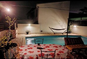 A poolside area with a table and chairs, a hammock, and a barbecue setup. - La Maison de Jo (Saint Paul)