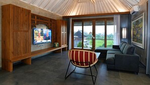 Ein modernes Wohnzimmer mit Fernseher, einer Couch, einem gestreiften Sessel und einem großen Fenster mit Blick auf Grünflächen.