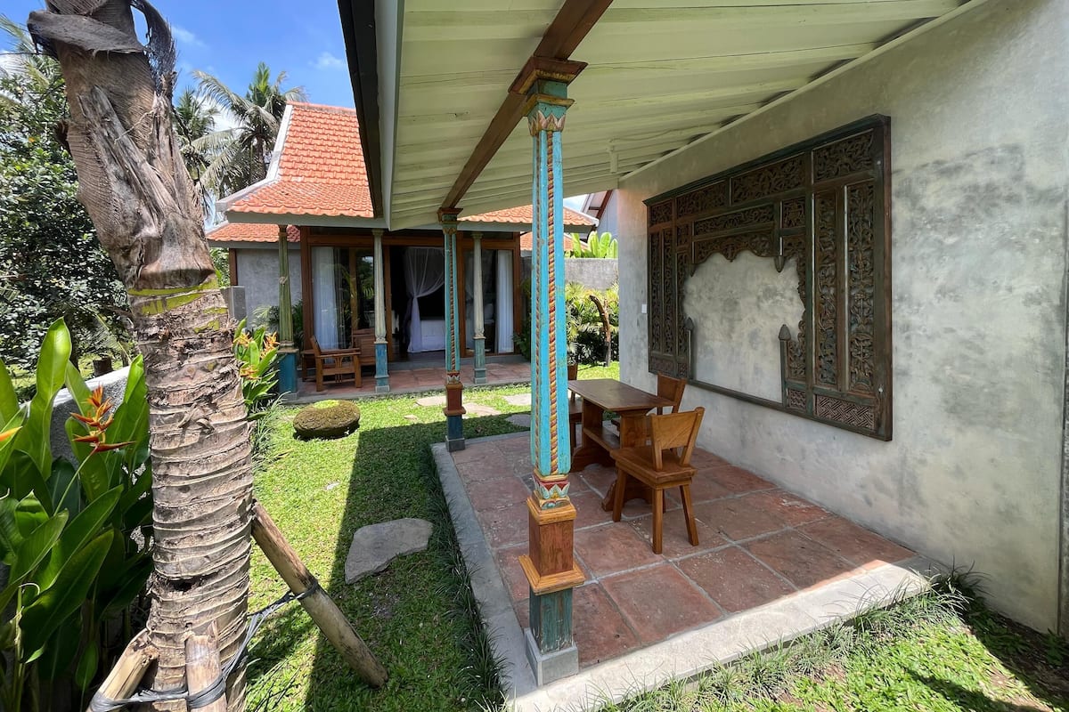 A traditional house with a tiled roof, a covered patio with a wooden table and chairs, and a decorative wall panel.