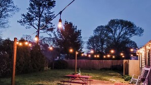 A backyard with a picnic table, string lights, and a wooden deck. - A relaxing family home with a fenced in backyard (Yarmouth)