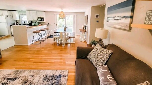A modern living room with a brown sofa, a patterned throw pillow, and a wooden floor. - A relaxing family home with a fenced in backyard (Yarmouth)