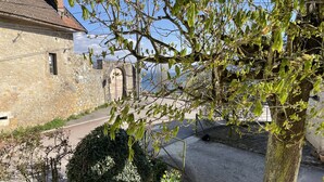 Un edificio in pietra con un cancello in metallo, un albero con foglie verdi e un cielo sereno.