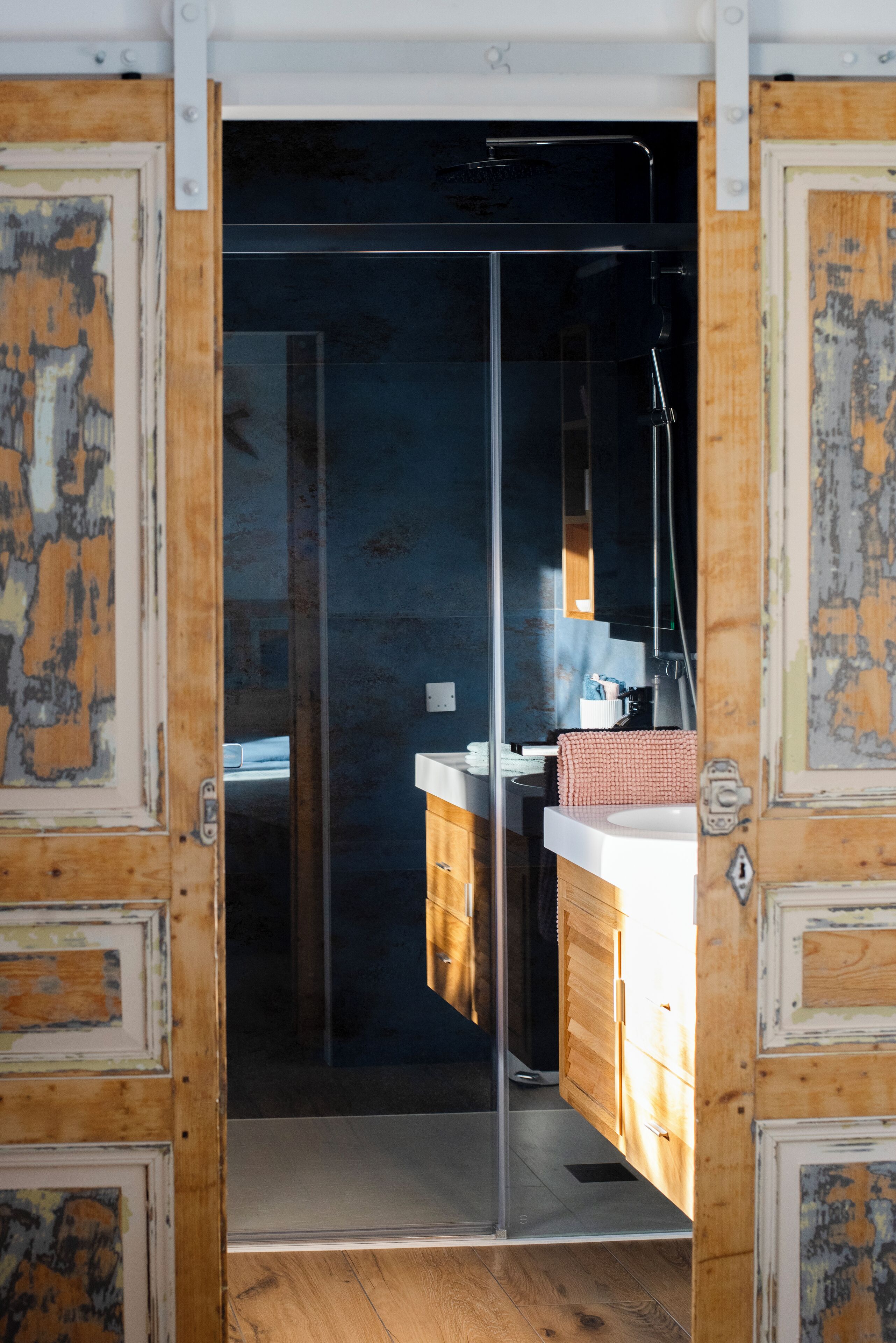 A bathroom with a glass shower door, wooden cabinets, and a white sink.