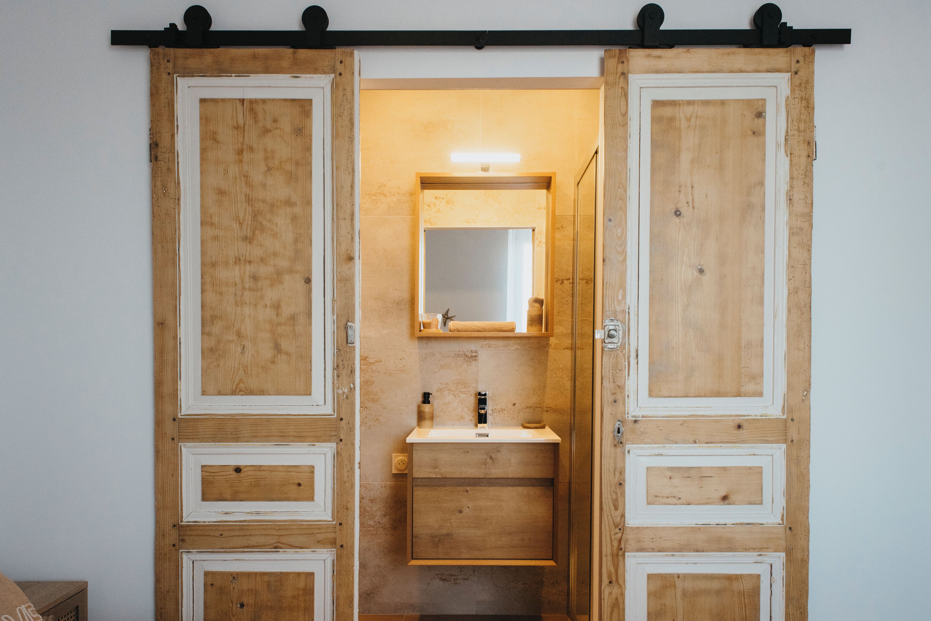 Eine Holztür mit Schiebevorhang, ausgestattet mit integriertem Waschbecken und Spiegel, zeichnet sich durch ein schlichtes, klares Design aus.