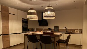 Una cucina moderna con isola centrale, luci a sospensione e sgabelli da bar.