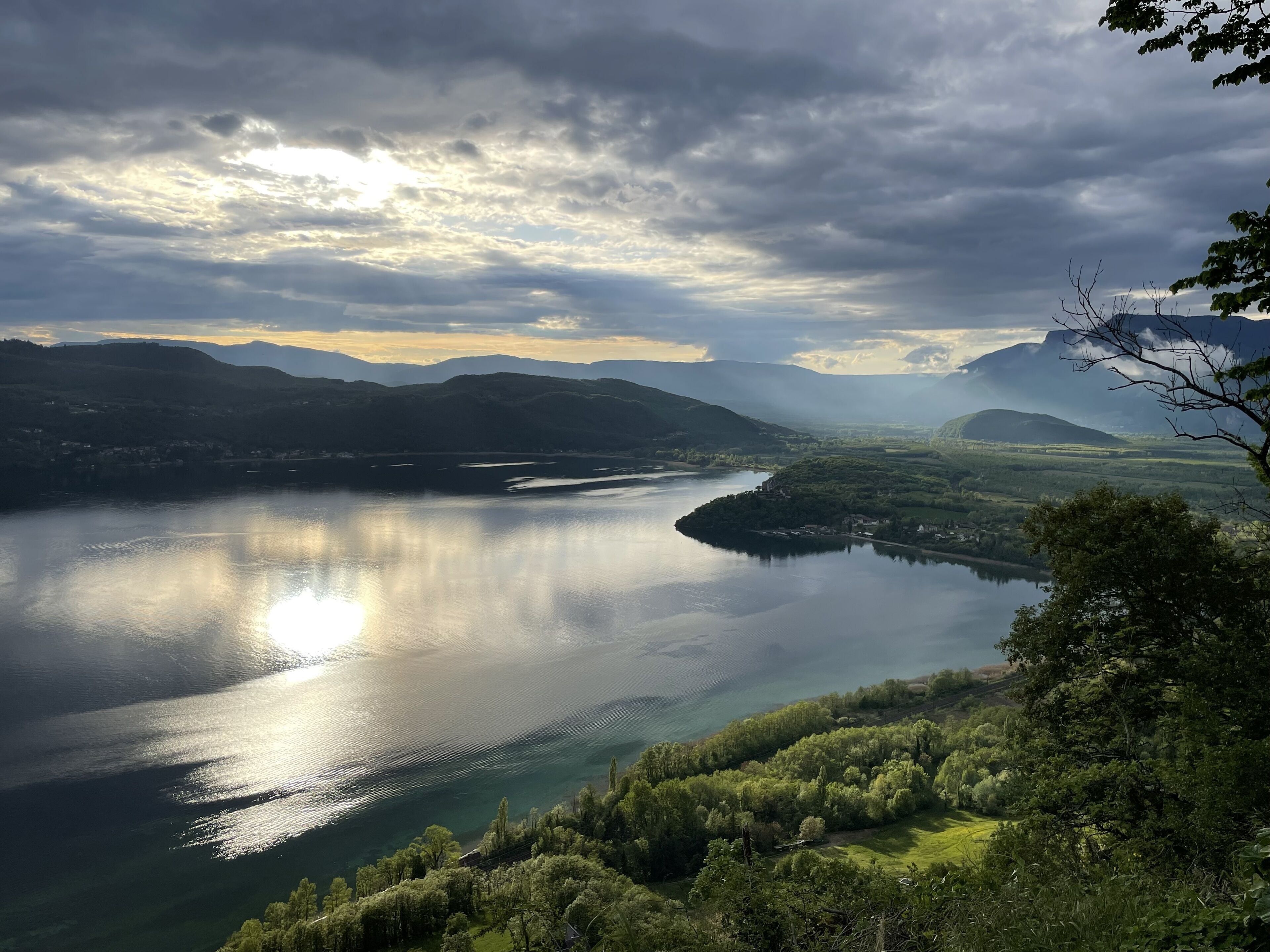Vista panorâmica de um lago rodeado por colinas e árvores, sob um céu claro.