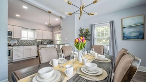 A dining area with a table set for six, surrounded by chairs, with a kitchen in the background. - 3 bedroom 1 bath house-Free Parking-10 min to EWR. (Irvington)