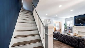 A staircase with wooden steps and white railings, leading to a living area with a dark-colored sofa and a fireplace. - 3 bedroom 1 bath house-Free Parking-10 min to EWR. (Irvington)