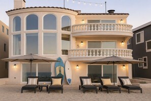 Una casa a più piani con un balcone, un'area salotto esterna e tavole da surf.