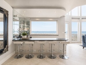 A modern kitchen with a bar area, large windows, and a view of the sea. - Luxury Oceanfront Vacation Home on Hollywood Beach (Oxnard)