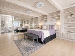 A bedroom with a large bed, a bench, a rug, and built-in shelving.