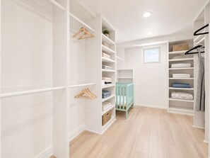 Un dressing accessible sans porte, avec des étagères blanches, un berceau turquoise et une fenêtre.