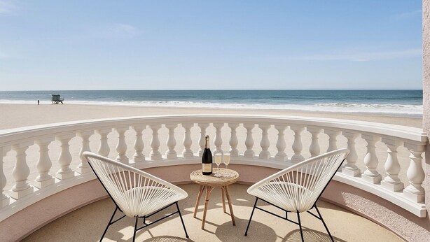 A balcony with two white wicker chairs, a bottle of champagne, and a small round table. - Luxury Oceanfront Vacation Home on Hollywood Beach (Oxnard)
