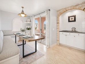 A modern kitchen with white cabinets, a stone archway, and a dining area with a table set for two. - Luxury Oceanfront Vacation Home on Hollywood Beach (Oxnard)